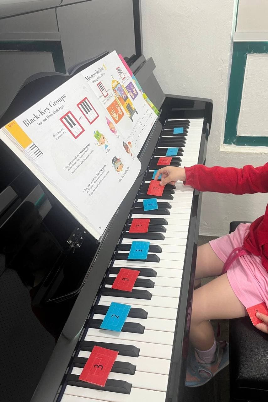 Child placing numbered cards on piano keys while following a lesson on black-key groups.
