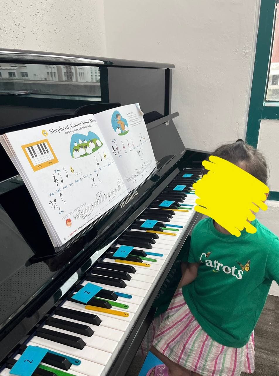Child sitting at a black piano with colorful key markers and open sheet music.