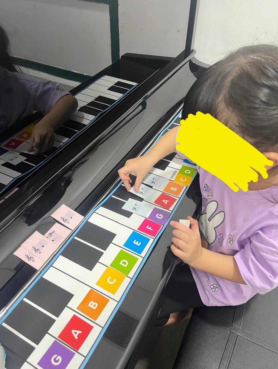 Child in purple shirt placing musical note cards on a colorful lettered piano guide.