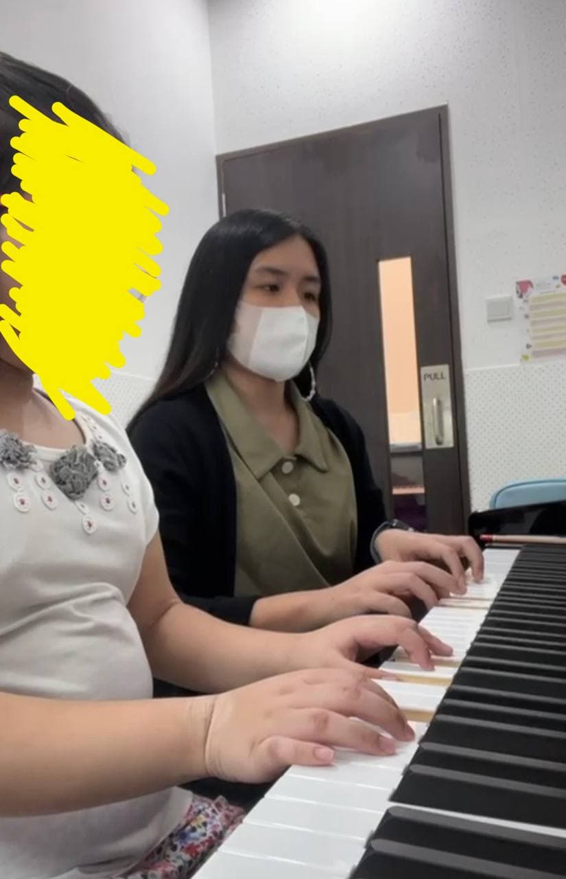 A masked woman and a young student playing a piano duet, focusing on their hands.